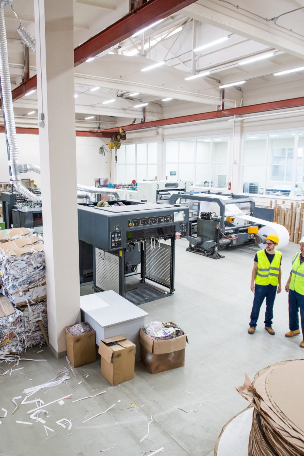 Workers of paper recycling factory wearing reflective vests standing in shop with packaged papers in cartoon and cutting machines